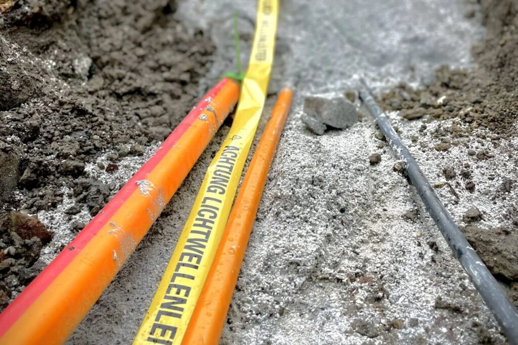 Orange Glasfaser-Leerrohre und gelbes Warnband Lichtwellenleiter in einer offenen Künette